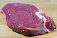 Ein rohes Stueck Steak liegt auf einer Holzunterlage.jpg