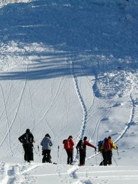 Eine Lawine rollt auf mehrere Skifahrer zu die den Berg hinaufschauen.jpg