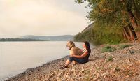 Eine Frau sitzt mit ihrem Hund am Flussufer und schauen beide auf das Wasser.jpg