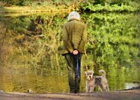 Eine aeltere Frau steht mit dem Ruecken zur Kamera mit ihrem Hund am Wasser.jpg