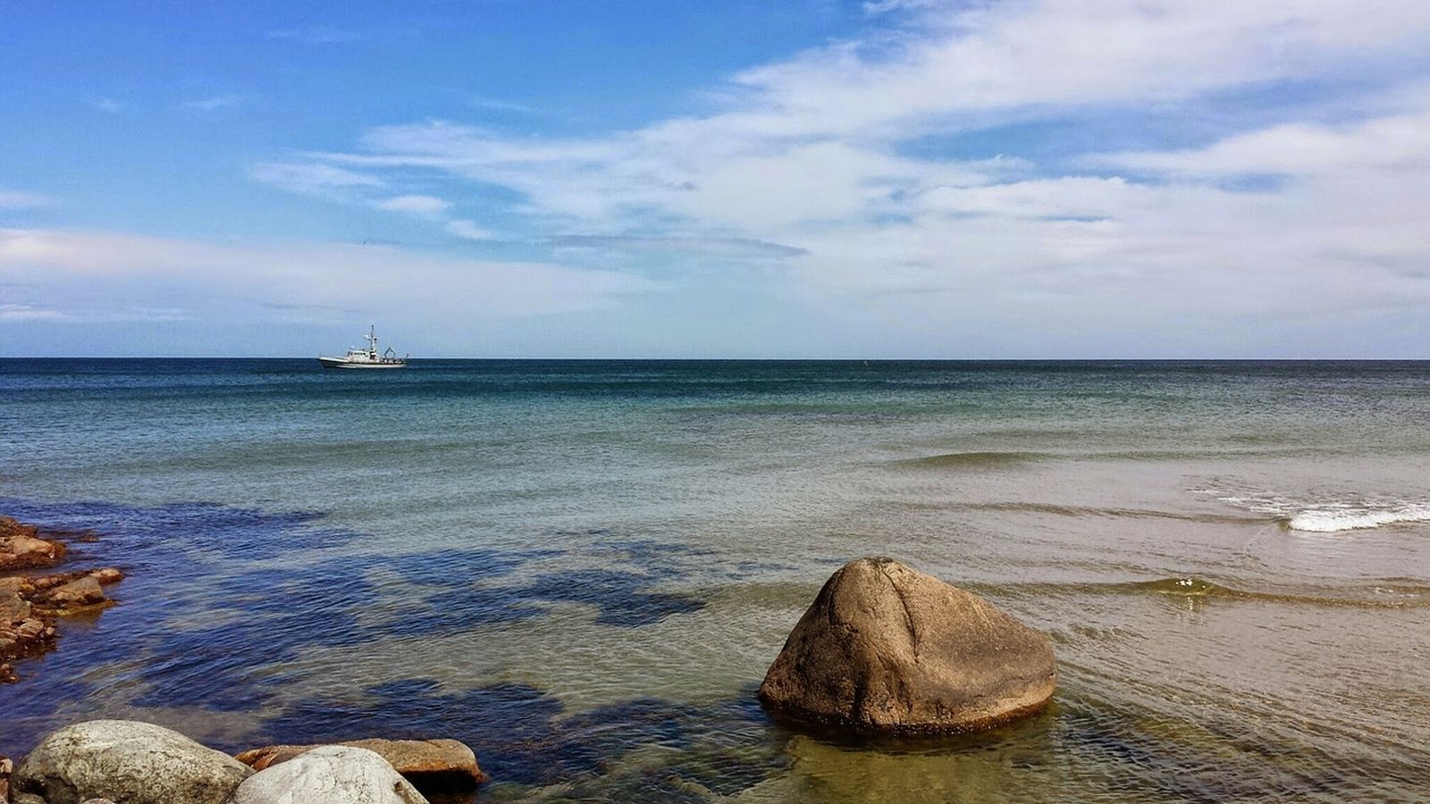 Ein Boot mitten im seichten Meer bei Bornholm in Dänemark vom Ufer aus aufgenommen