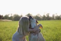 Maedchen mit langen blonden Haaren drueckt einen beigen Hund .jpg